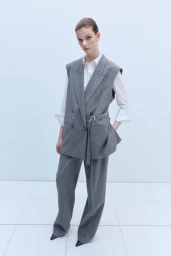 Model wearing a grey pinstripe sleeveless blazer vest with matching tailored trousers and a white shirt against a white backdrop.