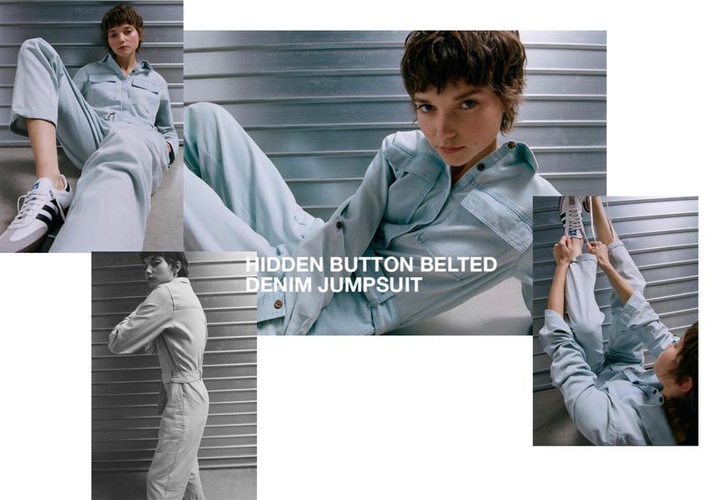 Fashion shot of a woman posing in a light denim jumpsuit, complemented by casual sneakers, against a corrugated metal backdrop.