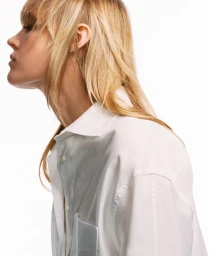 Side profile of a blonde woman wearing an oversized white button-down collared shirt against a white backdrop.