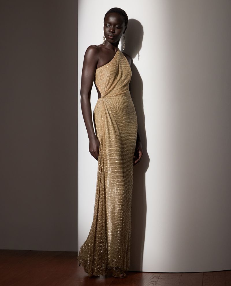 Elegant Black woman poses in a shimmering gold, one-shoulder gown, showcasing a blend of classic style and modern fashion in a studio setting.