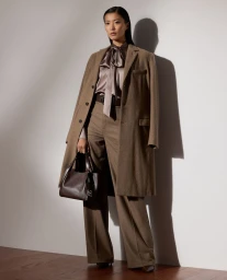 Amane Taniguchi posing in a tailored taupe overcoat, silk tie-neck blouse, wide-leg trousers, and leather handbag for Ralph Lauren.