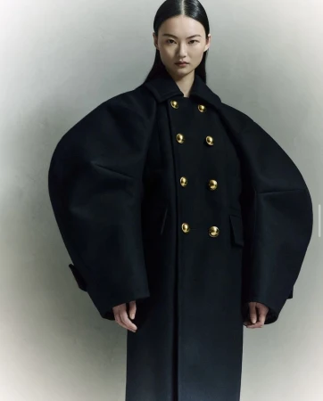 An Asian woman poses indoors wearing a long black double-breasted wool coat with gold buttons, styled with sleek, straight black hair.
