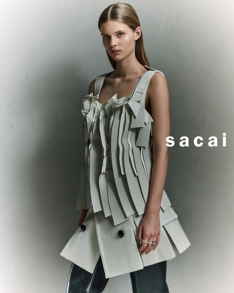 Fashion editorial shot of a woman with fair skin and light blonde hair wearing an avant-garde dress with layered geometric details.