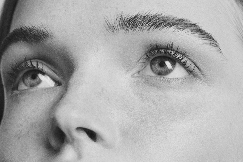 Close-up black and white studio portrait of a light-skinned adult woman's face, featuring her eyes, eyebrows, nose, and skin texture.