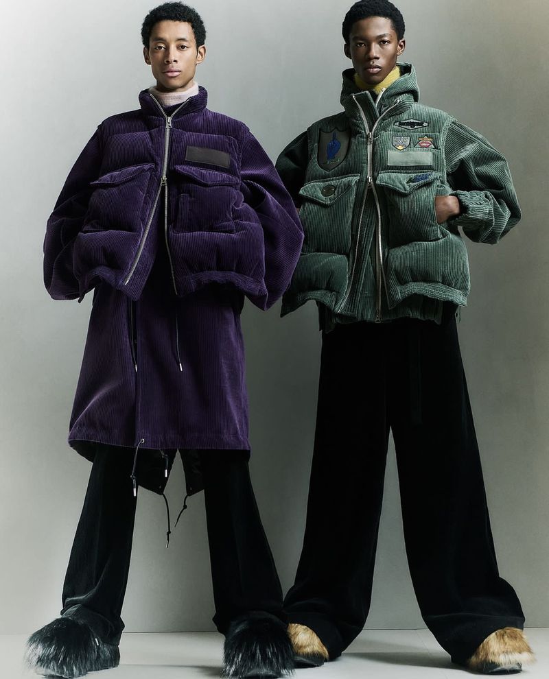 Two Black men in stylish puffer jackets and wide-leg pants pose in a studio with a neutral background. Fashionable and eye-catching studio shot.