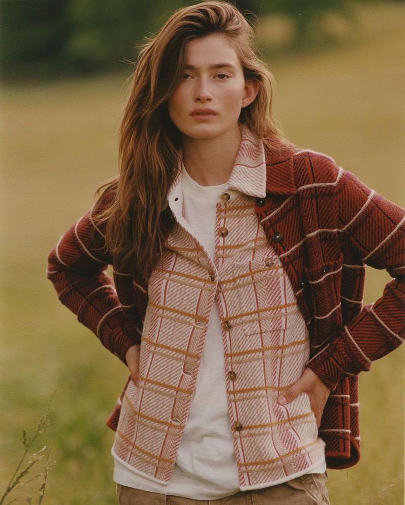 A woman poses outdoors in a fashionable, plaid flannel jacket over a white t-shirt, set against a soft-focus field.