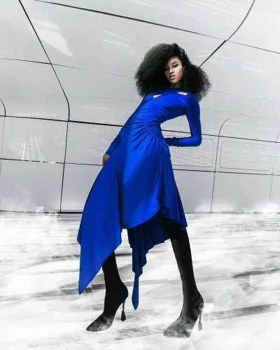 Model Inari Moore wearing an asymmetrical cobalt blue dress and black heel boots for Byblos Fall/Winter 2024 lookbook.