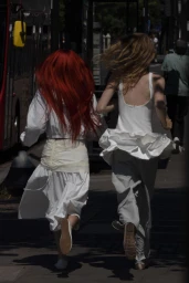 Rear view of two women with red and blonde hair running down an urban street in white outfits for Zara Woman AW24.