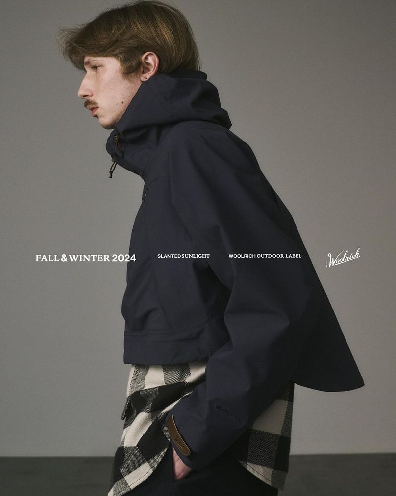 Fashion shot of a man in a dark blue hooded jacket over a plaid shirt against a grey backdrop, showcasing fall and winter apparel.