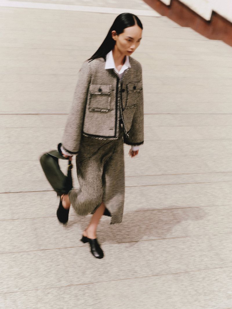 Model Ling Chen walks across a stone courtyard wearing a tailored tweed jacket and matching midi skirt for the ME+EM August Lookbook.