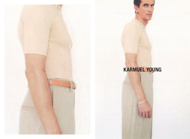 A slender adult male poses indoors in a tan short-sleeve shirt, light khaki pants, and tan belt against a white background in a fashion shot.