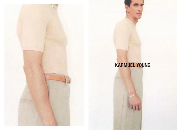 A slender adult male poses indoors in a tan short-sleeve shirt, light khaki pants, and tan belt against a white background in a fashion shot.