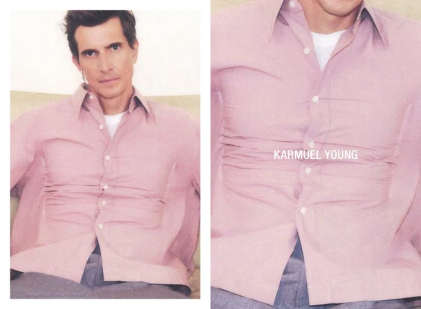 Portrait of an adult male wearing a pink button-down shirt and grey pants, casually posing indoors with a neutral background.