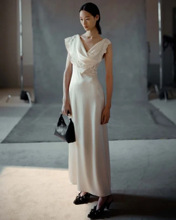 An Asian woman poses in a bright studio wearing a white dress and black heels, holding a black handbag, creating a fashion editorial image.