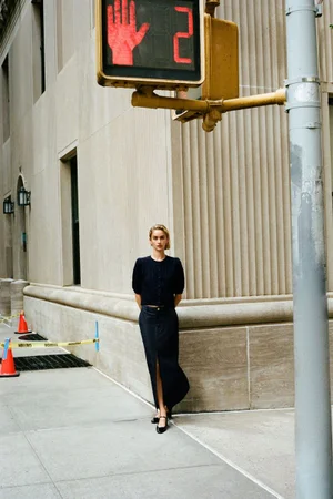Model standing on a city sidewalk next to a large building exterior beneath a traffic signal