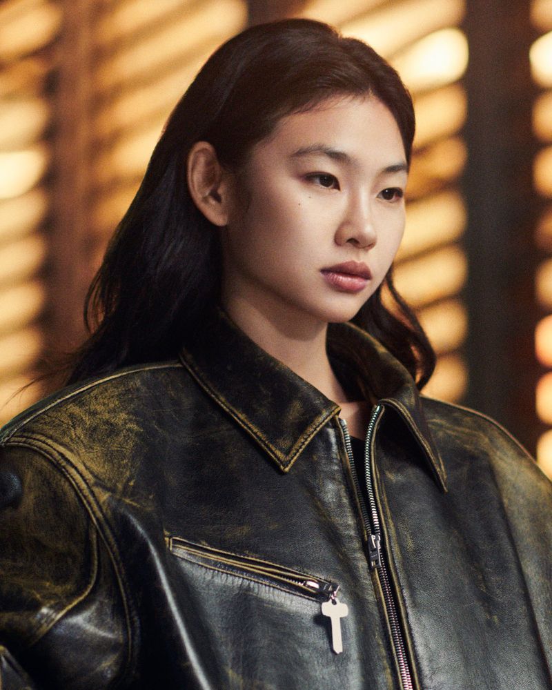 Close-up of an Asian woman with dark hair wearing a distressed black leather jacket, posing indoors against a warm-toned backdrop.