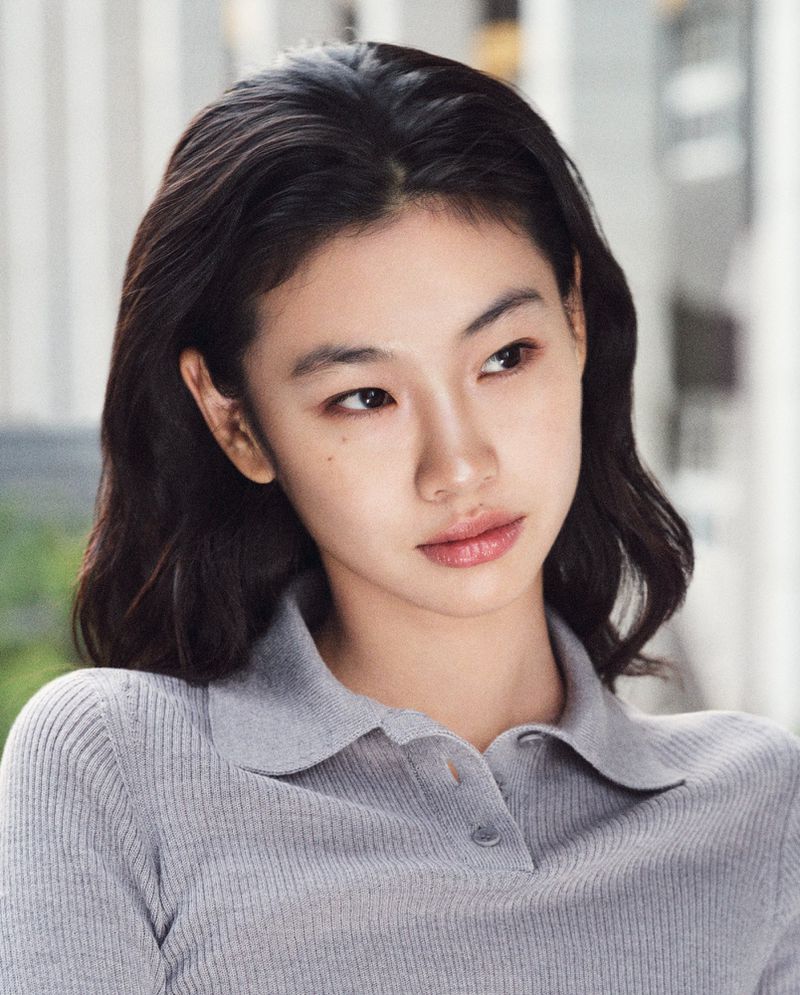Headshot of an Asian woman with dark hair in a grey collared top, looking slightly away from the camera in an outdoor setting.