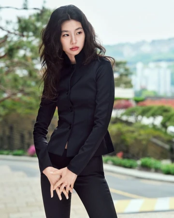 Portrait of a fashionable Asian woman in a black business suit with long hair, posing outdoors against a blurred green background.