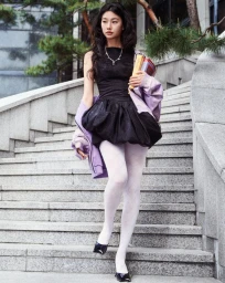 Hoyeon Jung walking down concrete stairs wearing a black dress, white tights, and a lavender jacket for SSENSE.