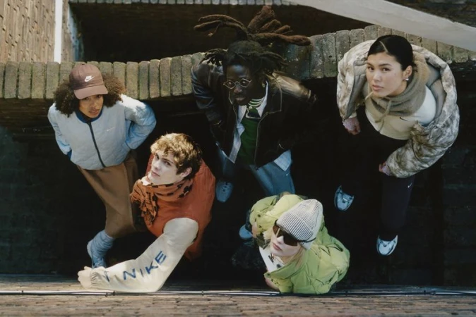 Eye-level shot of five diverse adults in stylish sportswear, including jackets and hats, against a modern concrete architectural background.