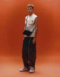 Model wearing utility vest, cargo pants, and crossbody bag standing against a solid orange background for Bershka