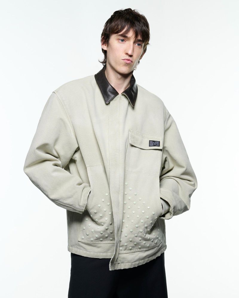 Portrait of a young adult man wearing an embellished jacket with leather collar on a white background in a fashion photography studio.