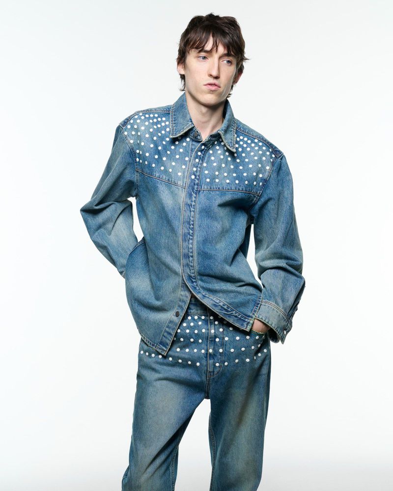 Male fashion model wearing denim shirt and jeans with white polka dot pattern in a full shot against a white background.