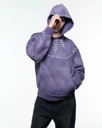 Model wearing an embellished purple hoodie and dark jeans against a white backdrop for Solid Homme x Stefan Cooke.