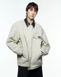 Young man in a pale green jacket with a dark leather collar against a plain white background