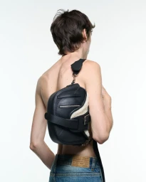 A man wearing a black leather bag and denim jeans photographed from behind against a plain white studio background.