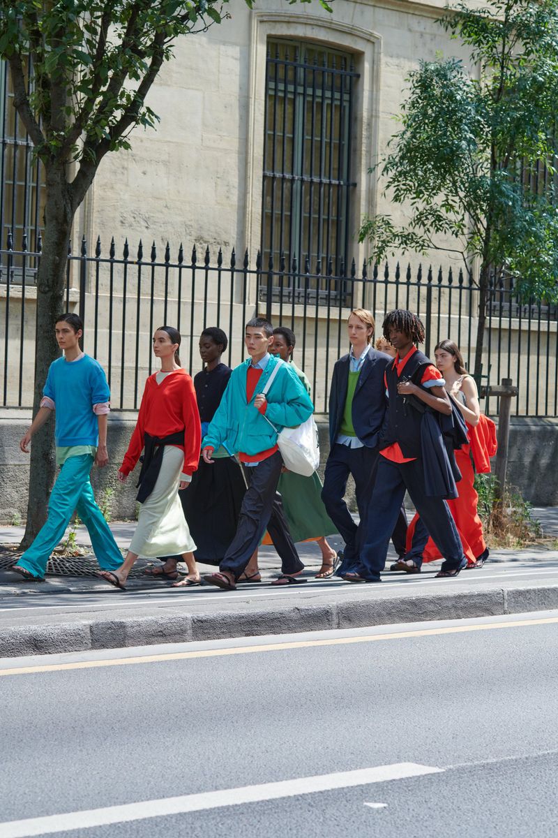 A group of eight diverse adults walking on a city street wearing colorful casual clothing, with urban architecture in the background.