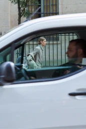 Model walking past a white car, viewed through the vehicle window, for Auralee SS24 campaign shot by Jack Day.