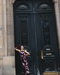 Model in a floral print dress and long burgundy gloves standing against a large dark double door