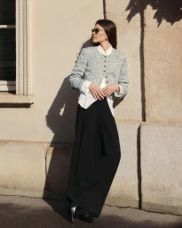 Model wearing a grey tweed jacket and black trousers leaning against an exterior building wall