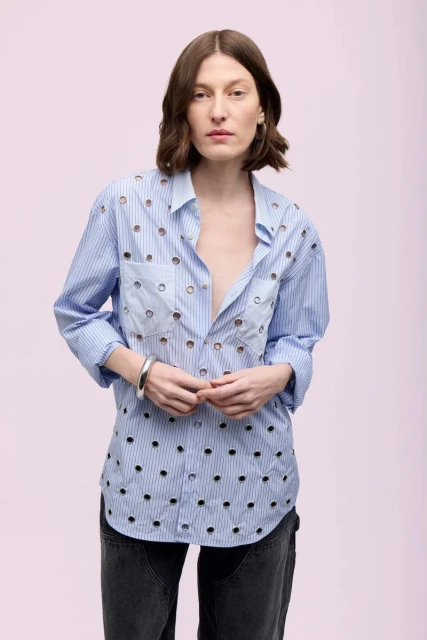 Adult woman posing indoors with neutral expression, wearing a pinstriped eyelet shirt and dark-wash jeans in a fashion studio shot.