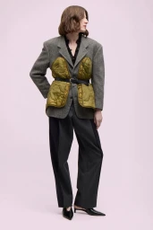 Model Jennae Quisenberry wears a belted grey blazer with olive quilted panels and wide trousers against a pale pink background.