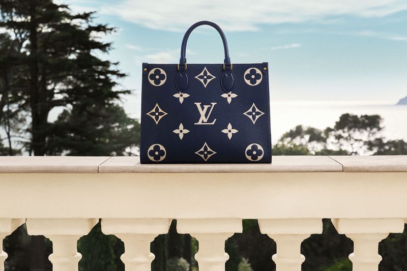 Elegant Louis Vuitton bag featuring iconic monogram design, positioned against a scenic backdrop of lush greenery and a serene blue sea.