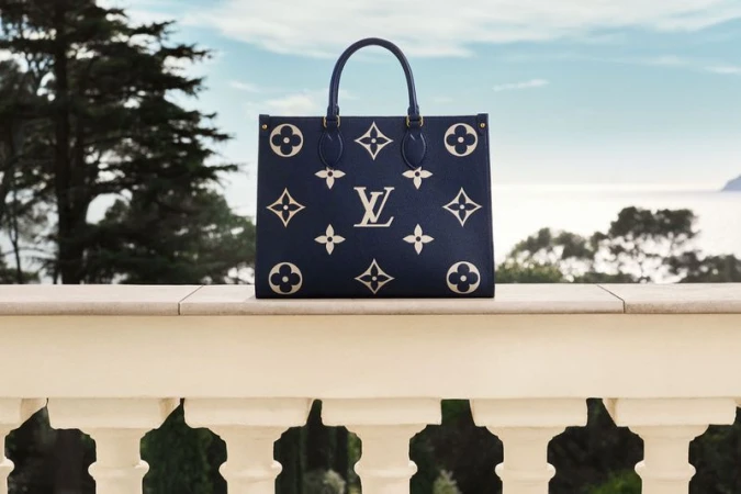 Elegant Louis Vuitton bag featuring iconic monogram design, positioned against a scenic backdrop of lush greenery and a serene blue sea.