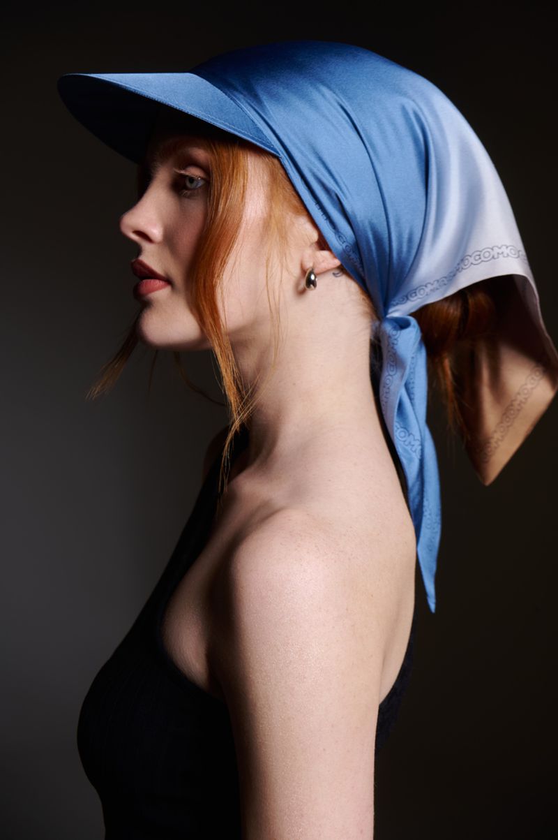 Portrait of a red-haired woman in a blue sun visor and black top, captured in a studio setting with focused lighting.