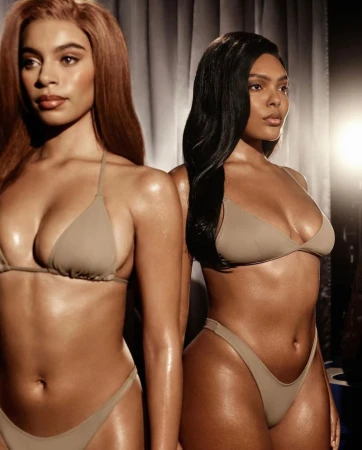 Two women wearing matching tan bikinis pose together in a studio with neutral background, showcasing swimwear and fashion.