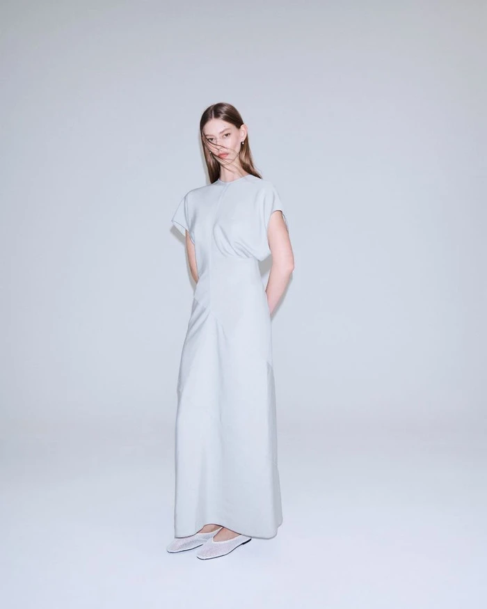 Model Ondria Hardin wearing a long grey dress against a white seamless background for COS