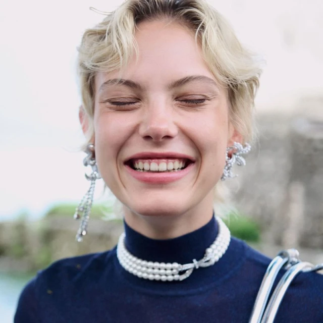 Smiling fair-skinned woman with blonde hair wears pearl choker and sparkling earrings. Close up fashion shot with blurred background.