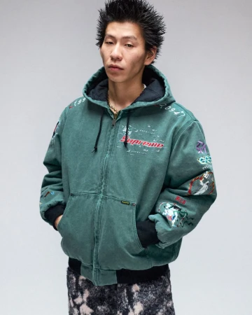 Asian man in a teal Supreme hooded jacket with graphics. He has spiky hair and is wearing a gold chain against a neutral background.