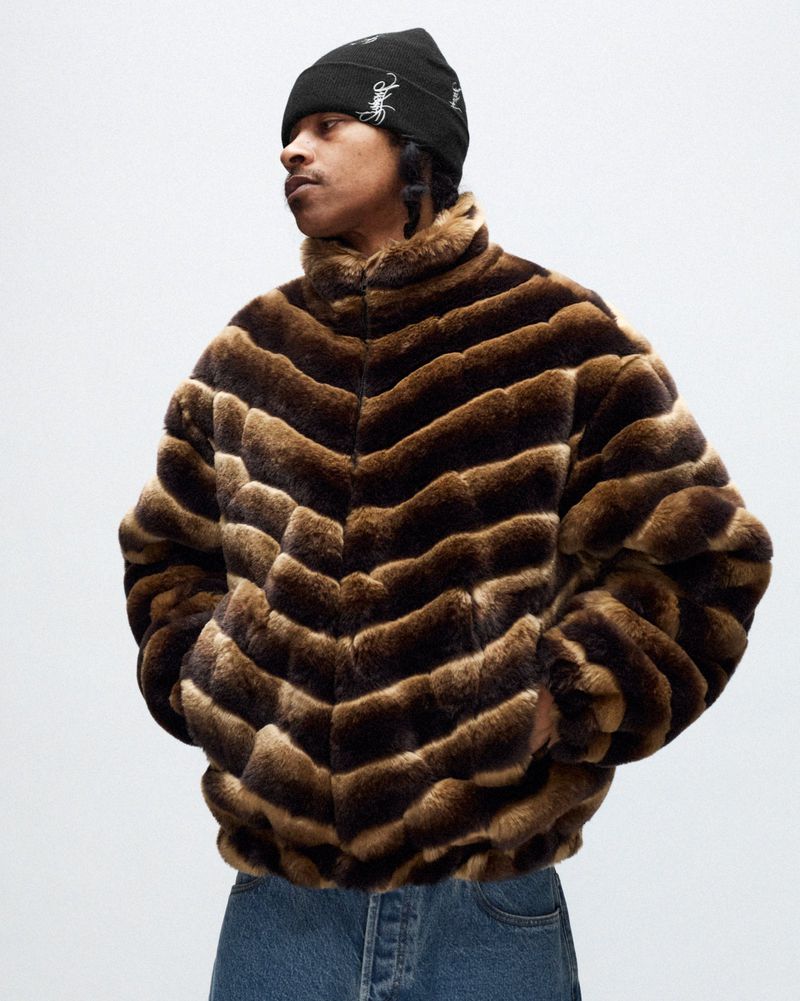 Adult male wearing a brown chevron-striped faux-fur jacket and a black beanie, photographed indoors against a plain white background.