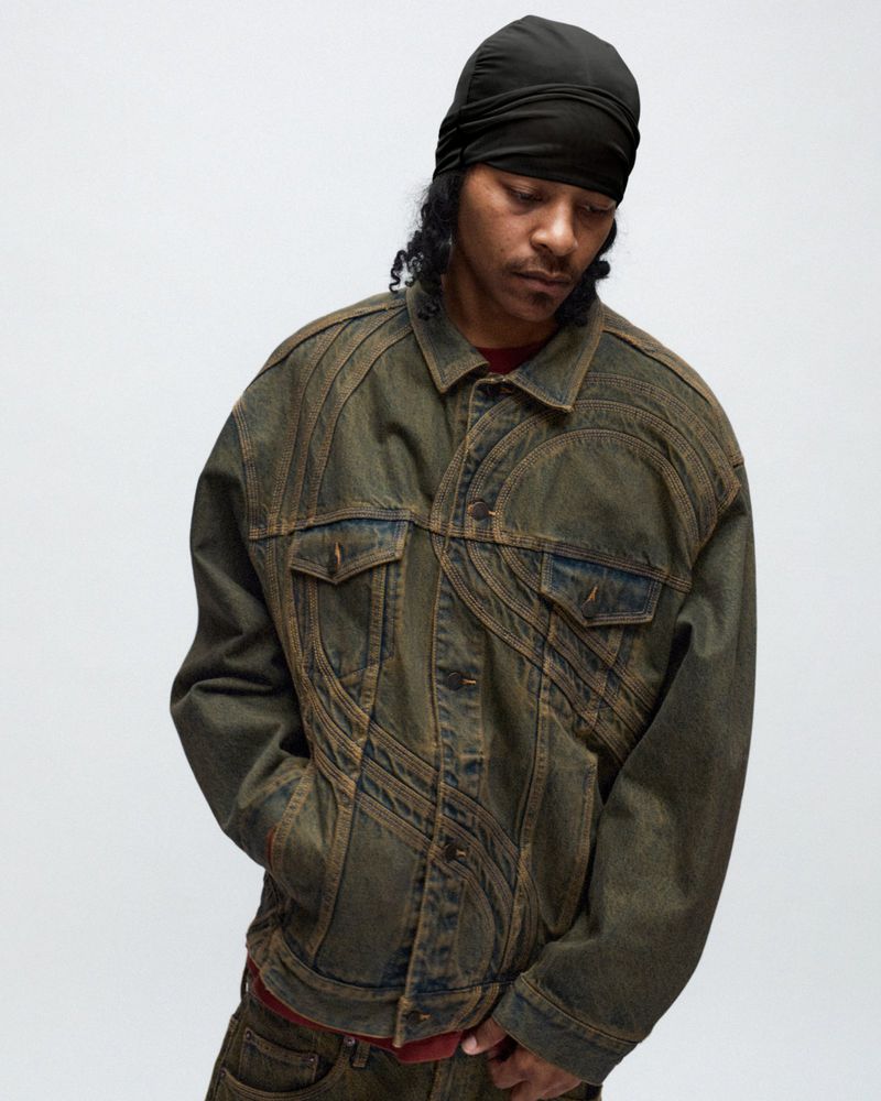 A man in a head wrap models an olive-green denim jacket and jeans against a white backdrop, showcasing the distressed fashion piece.