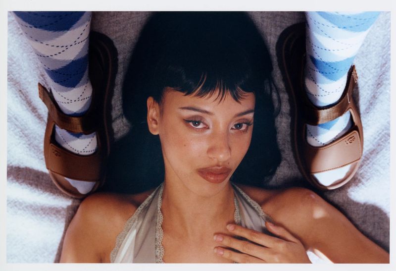 A young adult female lays on a textured surface wearing patterned socks, brown sandals, and a halter top, shot with soft, diffused light.