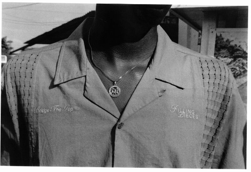 Black and white close-up photo of a person wearing a button-down shirt and pendant necklace outdoors, focusing on clothing and details.
