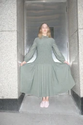 Model Jemima Kirke in a long sage green smocked dress standing in a stone doorway for Merlette Pre Fall 2025 Campaign