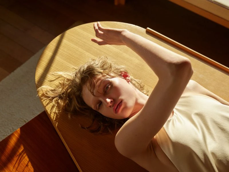 Eye-level shot of a blond woman lying on a wooden surface in natural light. A wooden rod rests on the surface behind her.