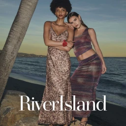 Two female models posing together on a sandy beach at sunset for the River Island spring summer campaign